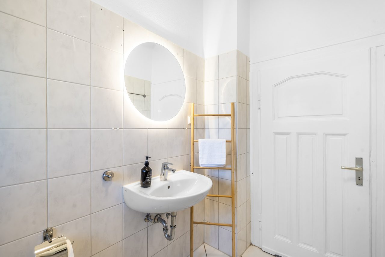 Badezimmer mit Waschbecken, rundem beleuchtetem Spiegel und Handtuchleiter