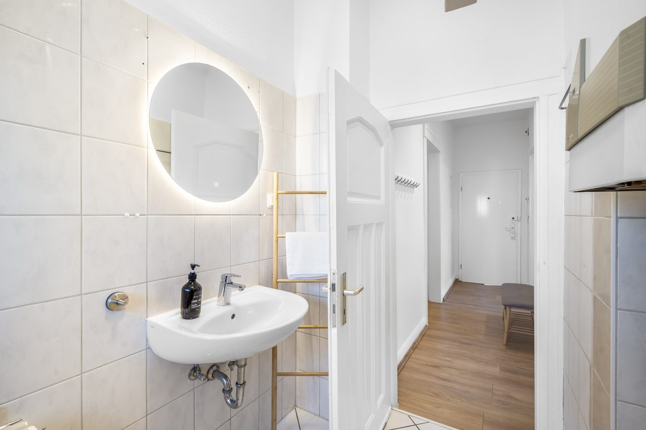 Badezimmer mit Waschbecken und rundem Spiegel, Blick in den Flur
