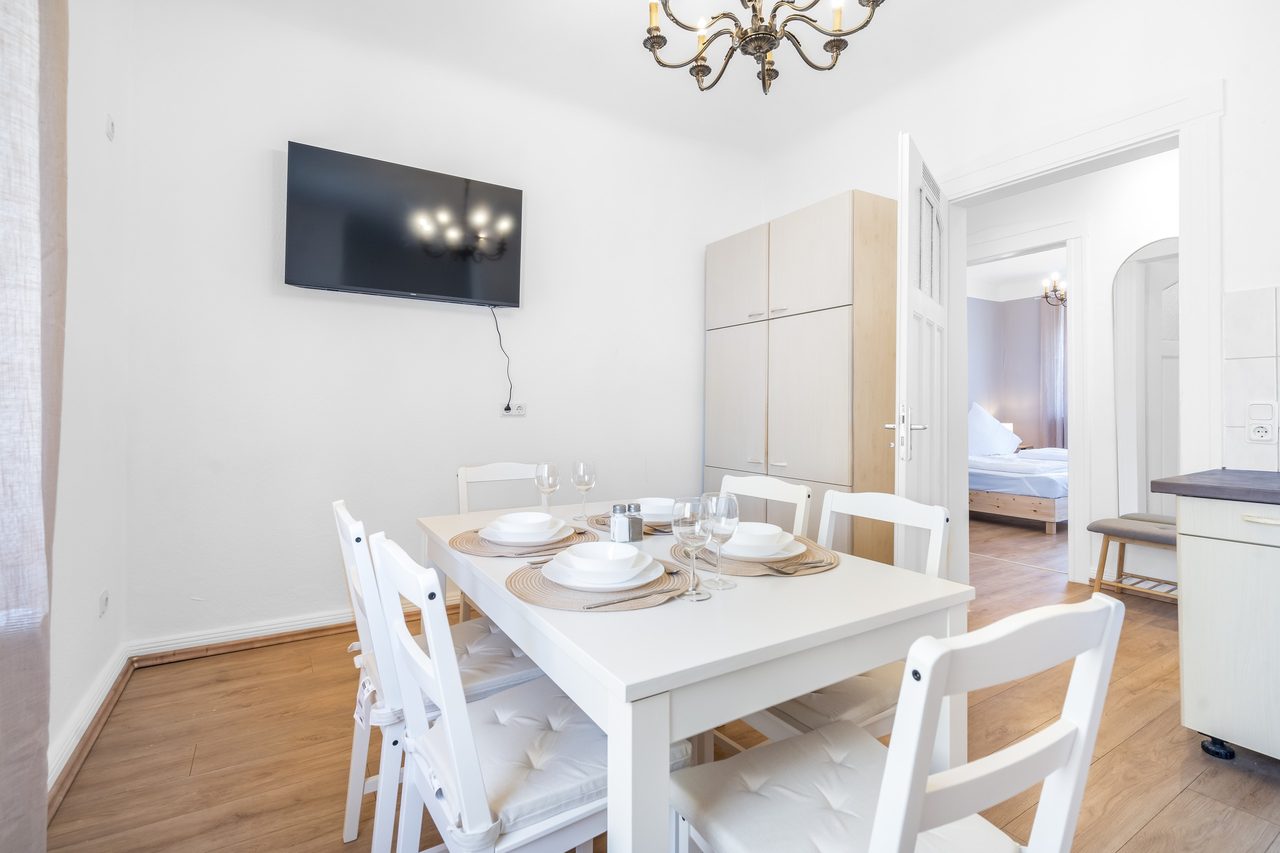 Essbereich mit gedecktem Tisch, weißen Stühlen und Fernseher an der Wand