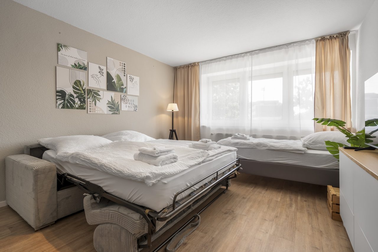 Wohnraum mit ausgezogenem Schlafsofa und Doppelbett vor großem Fenster
