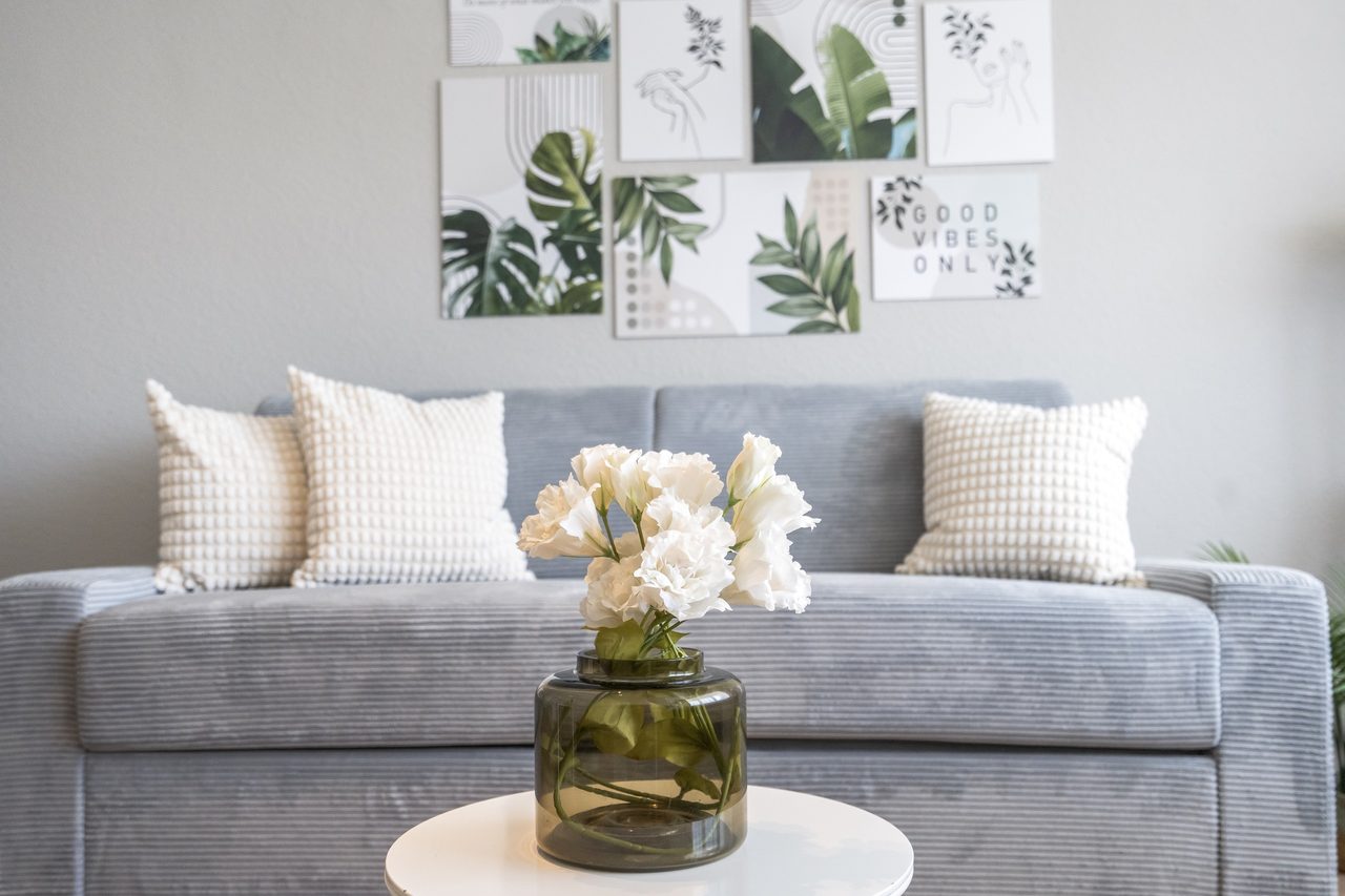Graues Sofa mit Kissen, Blumenvase und Pflanzenbildern an der Wand