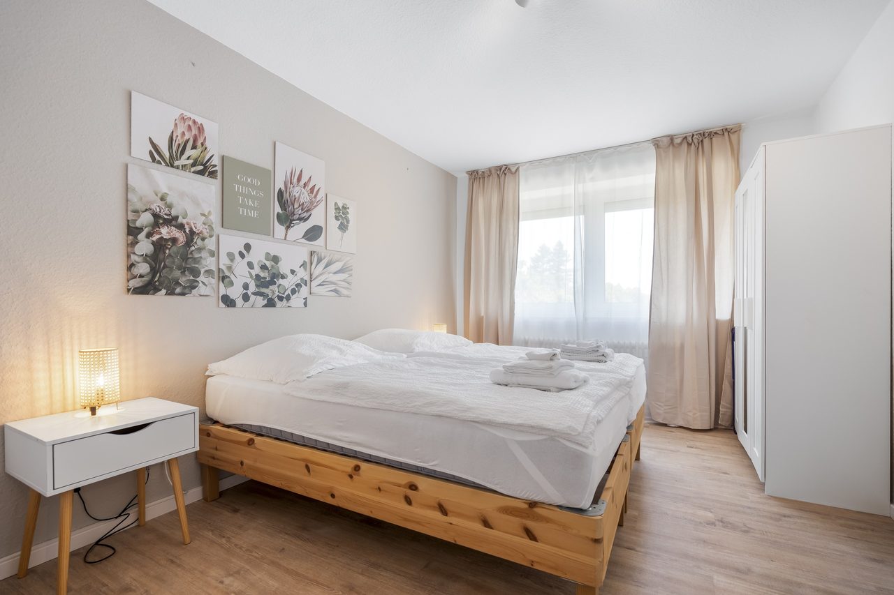 Schlafzimmer mit Holzbett, weißer Bettwäsche und Nachttisch mit Lampe