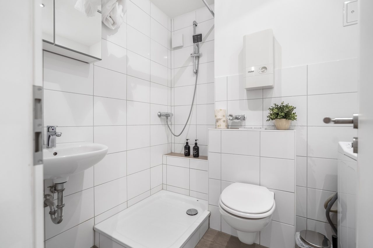 Badezimmer mit Dusche, Waschbecken und Wand-WC, weiß gefliest