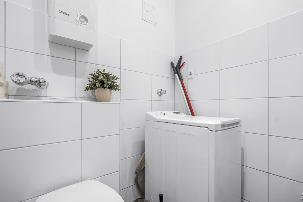 Badezimmer mit Waschmaschine, weißen Fliesen und Pflanze