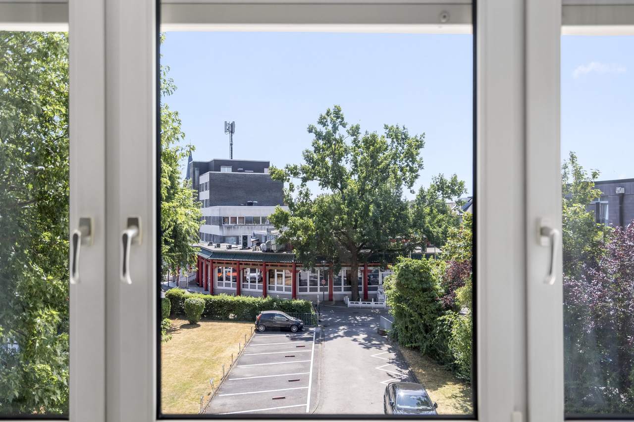 Blick aus dem Fenster auf Bäume, Gebäude und Parkplatz